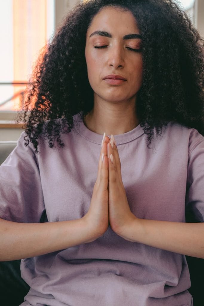 Peaceful woman in a crew neck t-shirt meditating indoors with hands together.