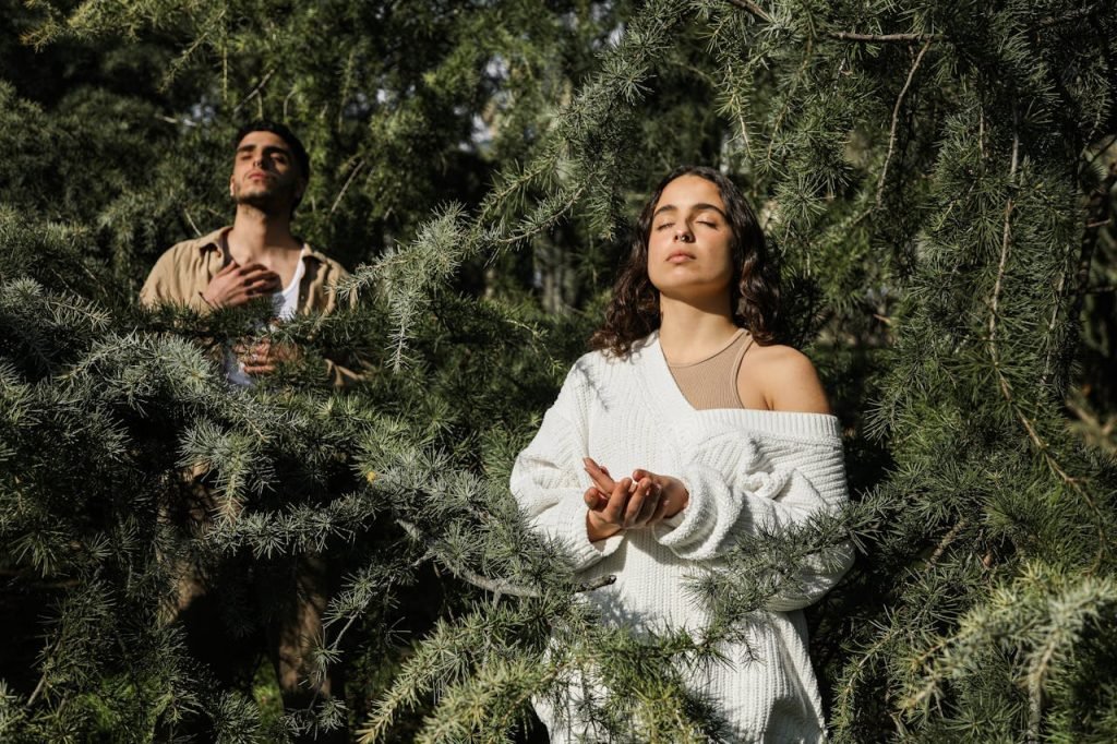 Two adults meditate peacefully amidst lush green trees in a forest.
