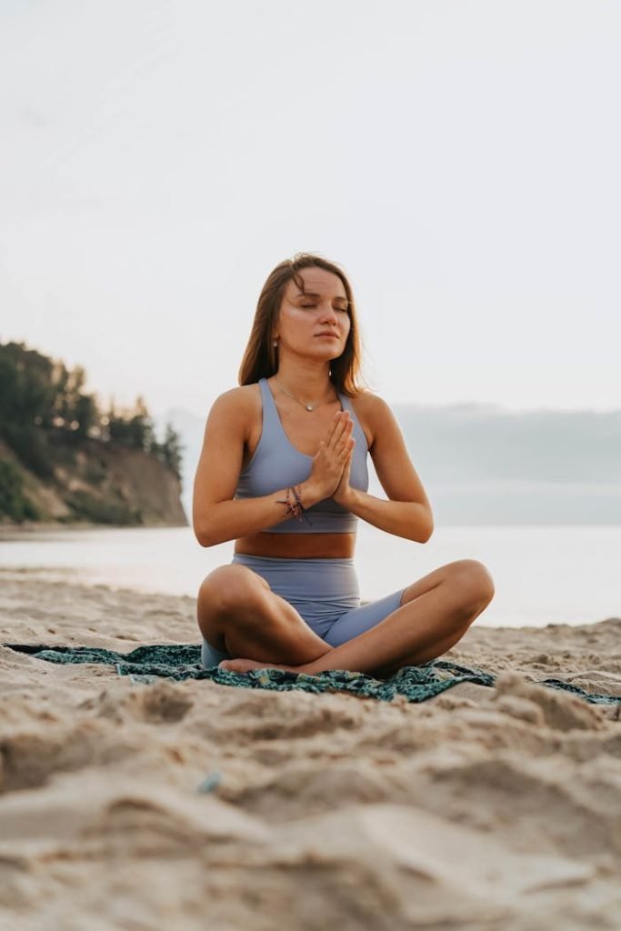 Woman meditates in activewear on a serene beach, embodying tranquility and mindfulness.