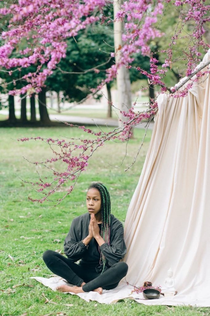 Woman practicing meditation outdoors under blooming trees with vibrant flowers.