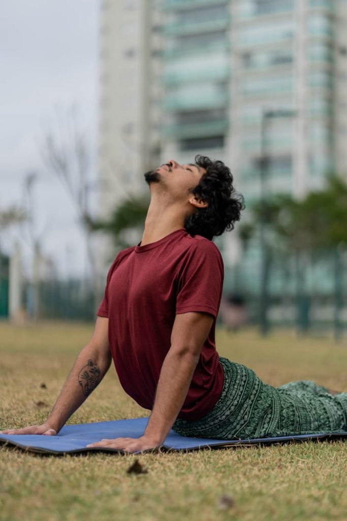 Adult man doing outdoor yoga on a blue mat in an urban park setting