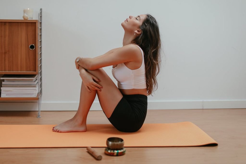 Woman meditating on orange yoga mat indoors, emphasizing relaxation and mindfulness.